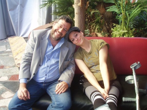 Marco Passarello e Amanda Palmer seduti su un divano, lei con la testa appoggiata sulla spalla di lui. Accanto ad Amanda è appoggiata una stampella.